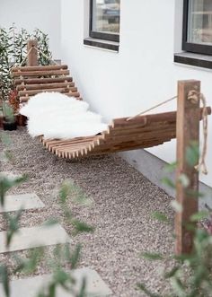 a bench made out of wood and rope sitting on the side of a building next to potted plants