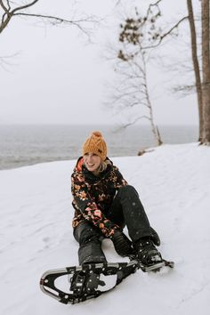 a person sitting in the snow on their skis with trees and water in the background