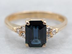 an emerald and diamond ring with two diamonds on the side, set in yellow gold