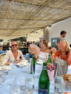 several people sitting at a table with drinks and water in front of them, under an umbrella