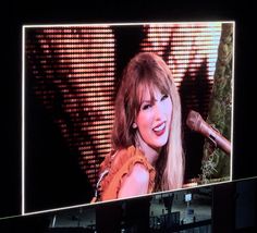 a woman with long hair standing in front of a microphone on a large television screen