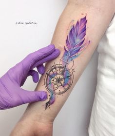 a person with purple gloves and tattoos on their arm holding up a tattoo design that looks like a feather