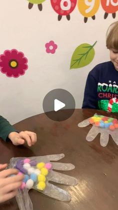 two young boys sitting at a table making handprints out of plasticine gloves