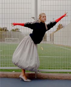 a woman is standing on one leg with her arms spread out in the air while wearing a skirt and heels