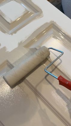 a paint roller is being used to paint a piece of white furniture with red handles