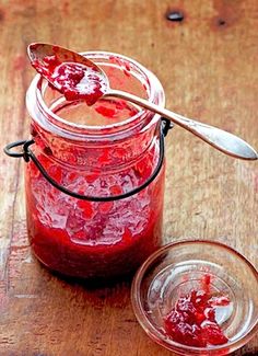 a jar filled with jam sitting on top of a wooden table next to a spoon