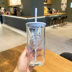 a person holding up a clear cup with a straw in it on a wooden table