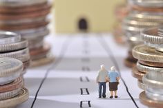 two miniature people standing on top of a table next to stacks of money and coins