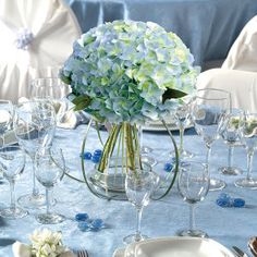 the table is set with wine glasses, plates and vases filled with hydrangeas