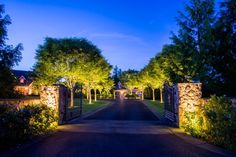 an entrance to a home at night with lights on and trees lining the walkways