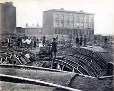 an old black and white photo of people standing in the middle of a building yard