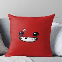 a red pillow sitting on top of a couch next to a white pillow with a smiling face