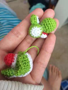 someone is holding two crocheted ornaments in their hands, one has a green and white mouse on it