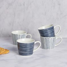 three coffee cups sitting on top of a counter next to cookies and crackers in front of them