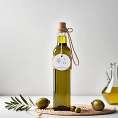 an olive oil bottle with some green olives on the side and a rope around it