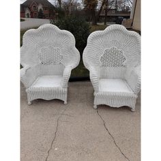 two white wicker chairs sitting next to each other on the sidewalk in front of a house