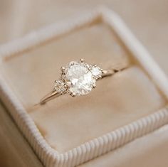 an engagement ring sits in a box on top of a cloth covered cushioned surface