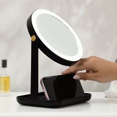 a person holding a cell phone in front of a magnifying mirror on a table