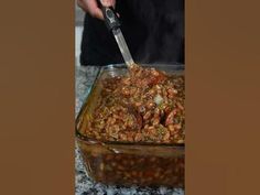 a person cutting up food in a glass casserole dish on a granite countertop