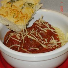 a white bowl filled with meat and cheese on top of a red place mat next to a slice of bread