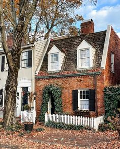 an old brick house with white trim and black shutters on the front, surrounded by autumn leaves