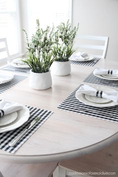 the table is set with black and white placemats, napkins, and potted plants