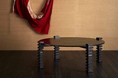 a table and chair in front of a wall with a red cloth hanging on it