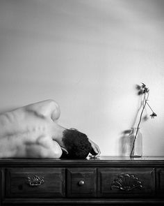 a person laying on top of a dresser next to a vase