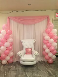 a chair and some balloons in front of a white wall with pink drapes on it