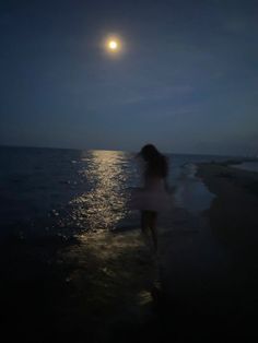 a woman is walking on the beach at night