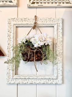 a white frame hanging on the wall with flowers in it