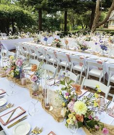 a long table is set up with place settings and flowers on it for an outdoor wedding reception