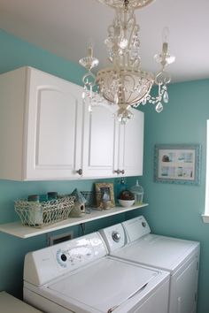 a washer and dryer in a small room with blue walls, white cabinets and chandelier