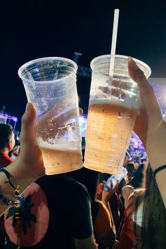 two people holding up plastic cups with drinks in them at an outdoor music festival or gathering