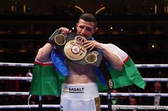 a man standing next to a boxing ring holding up a gold and black belt in his right hand