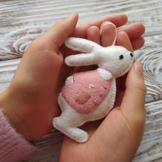 a hand holding a small stuffed animal in it's left hand on a wooden surface