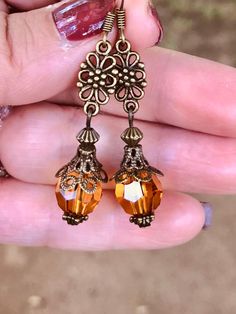 a person is holding some kind of earring in their hand and it has an orange crystal