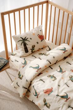 an unmade bed with dinosaurs and palm trees on it, next to a wooden crib