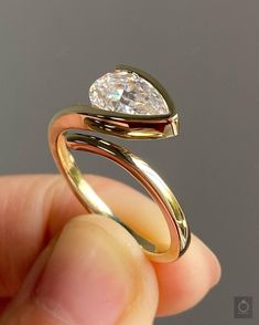 a hand holding a gold ring with a pear shaped diamond