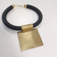 This stunning African-inspired choker necklace features a bold and elegant design. The necklace is crafted with a thick black leather band that sits comfortably around the neck. At the center, a large, hammered brass pendant adds a touch of luxury and tradition, reflecting the rich cultural heritage of African craftsmanship. The combination of leather and golden brass creates a striking contrast, making this piece both modern and timeless. Perfect for those looking to make a statement, this neck Modern Leather Choker Jewelry, Modern Black Metal Choker, Bold Outfits, Sculptural Jewelry, Oversized Earrings, Hammered Brass, Bib Necklaces, Geometric Necklace, African Jewelry