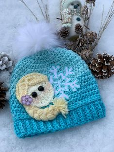 a crocheted hat with a doll on it and pine cones in the background