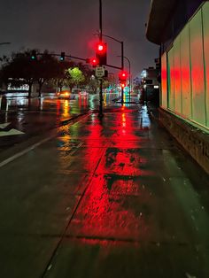 a red traffic light sitting on the side of a wet road at night with buildings in the background