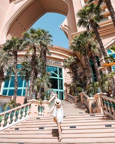 a woman is walking down the stairs in front of a building with palm trees on it