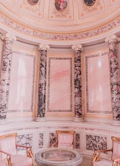 an ornate room with pink chairs and paintings on the walls, in front of a round table