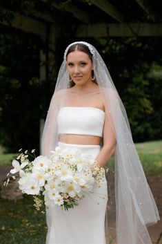 a woman in a white wedding dress holding a bouquet of flowers and wearing a veil