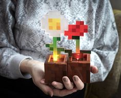 a woman holding two small lego plants with candles in it's hands, both made out of different colored blocks