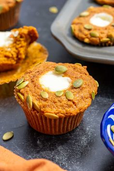 pumpkin spiced muffins with cream cheese and pumpkin seeds in the middle on a black surface