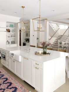 a large kitchen with white cabinets and an island in front of the stairs is decorated with greenery