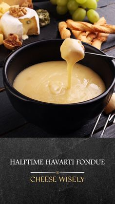 cheese fondue being drizzled into a bowl with grapes in the background