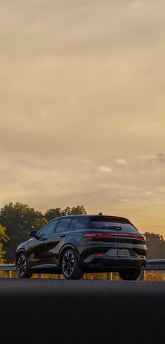 a black car is parked on the side of the road with trees in the background